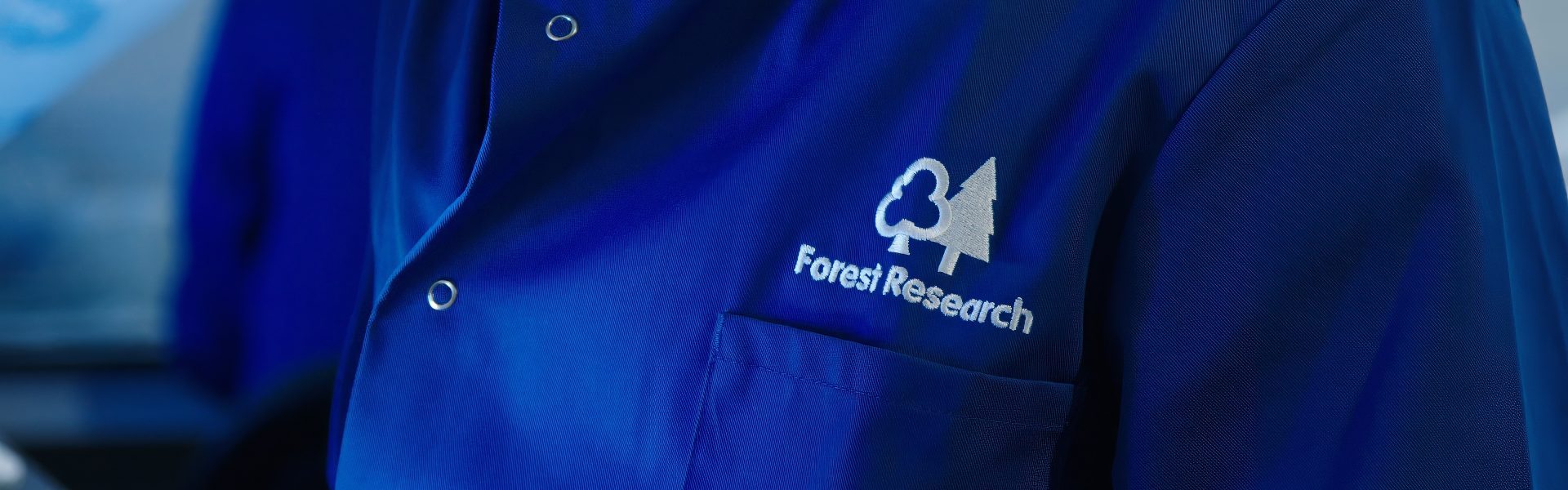 A Forest Research scientist wears a blue lab coat with the organisation logo visible.