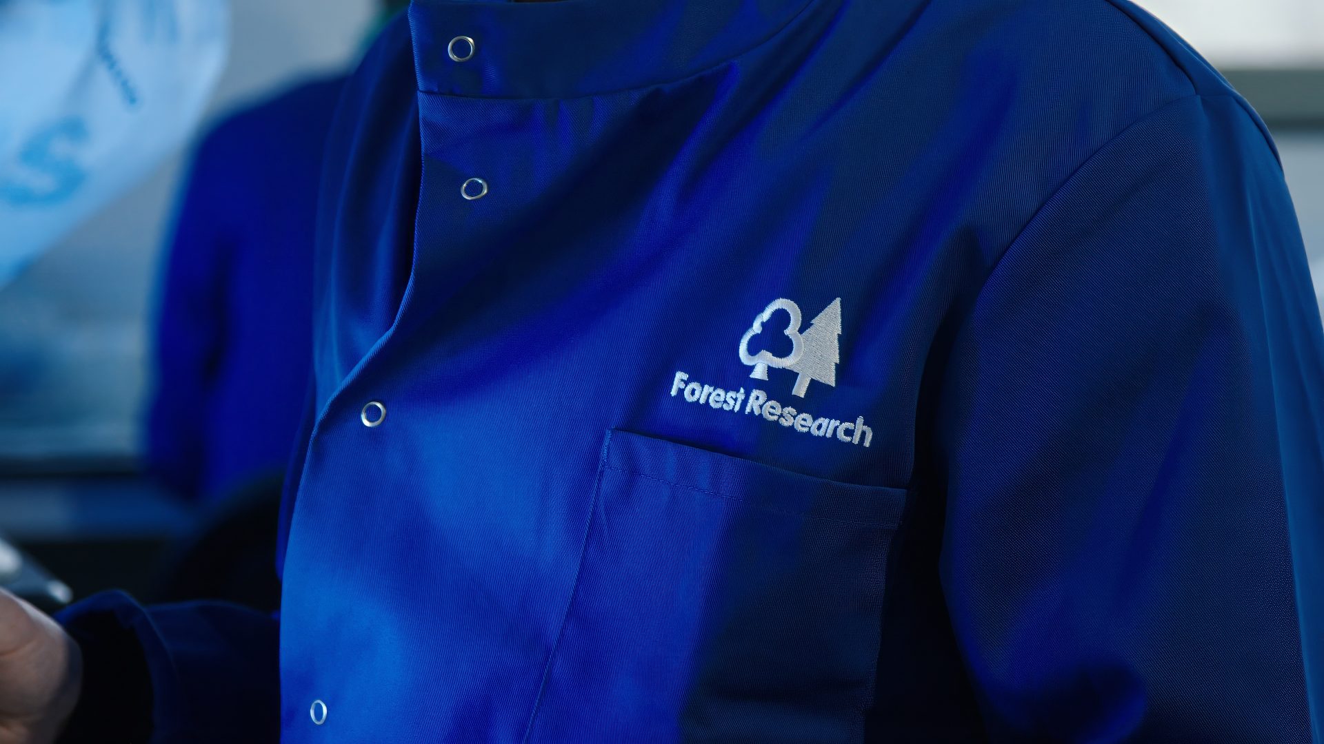 A Forest Research scientist wears a blue lab coat with the organisation logo visible.