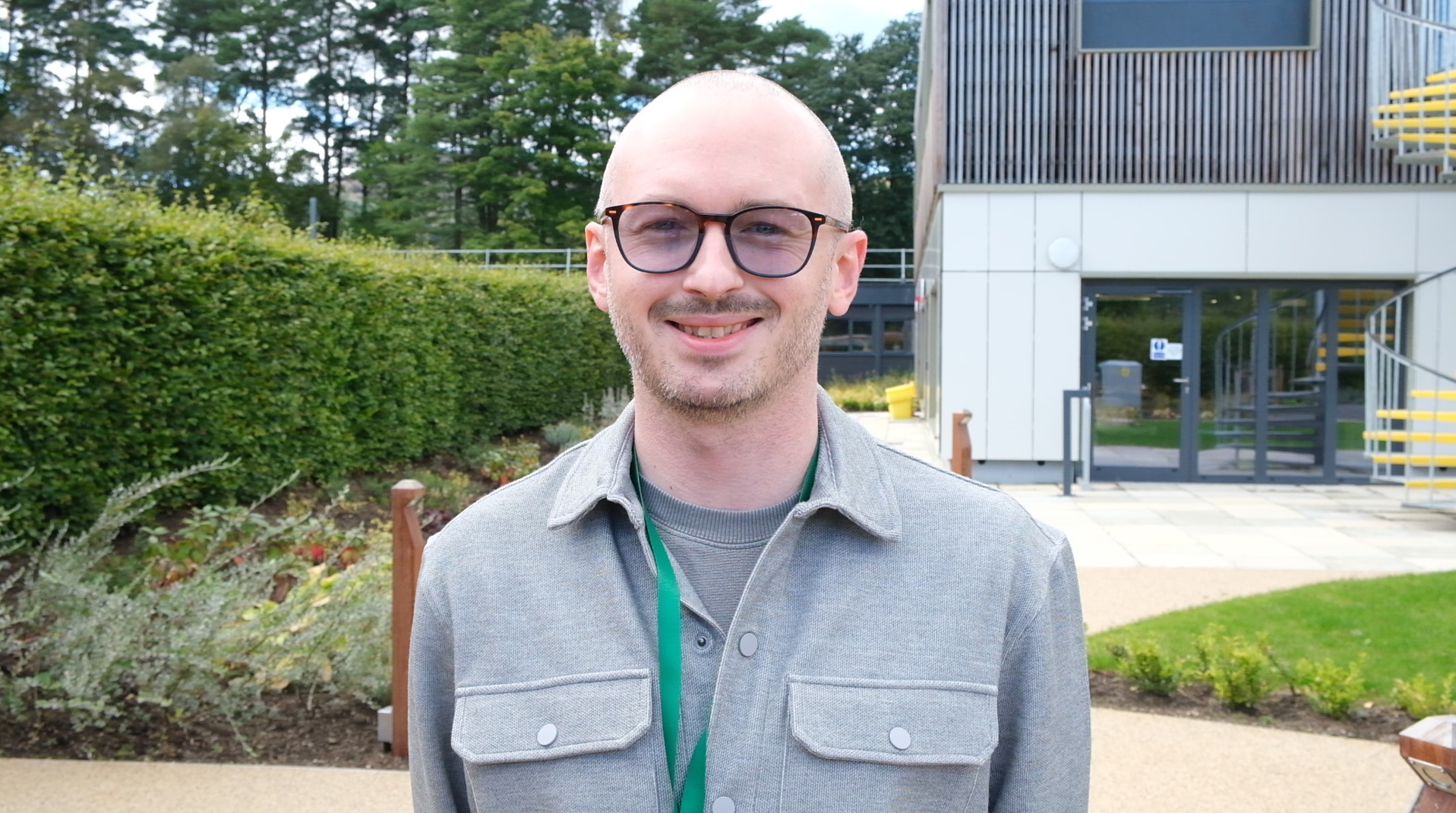 A photo of Alex facing the camera smiling. The NRS offices are in the background.