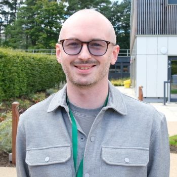 Alex MacPherson profile picture, he looks at the camera, and the NRS offices are in the background.