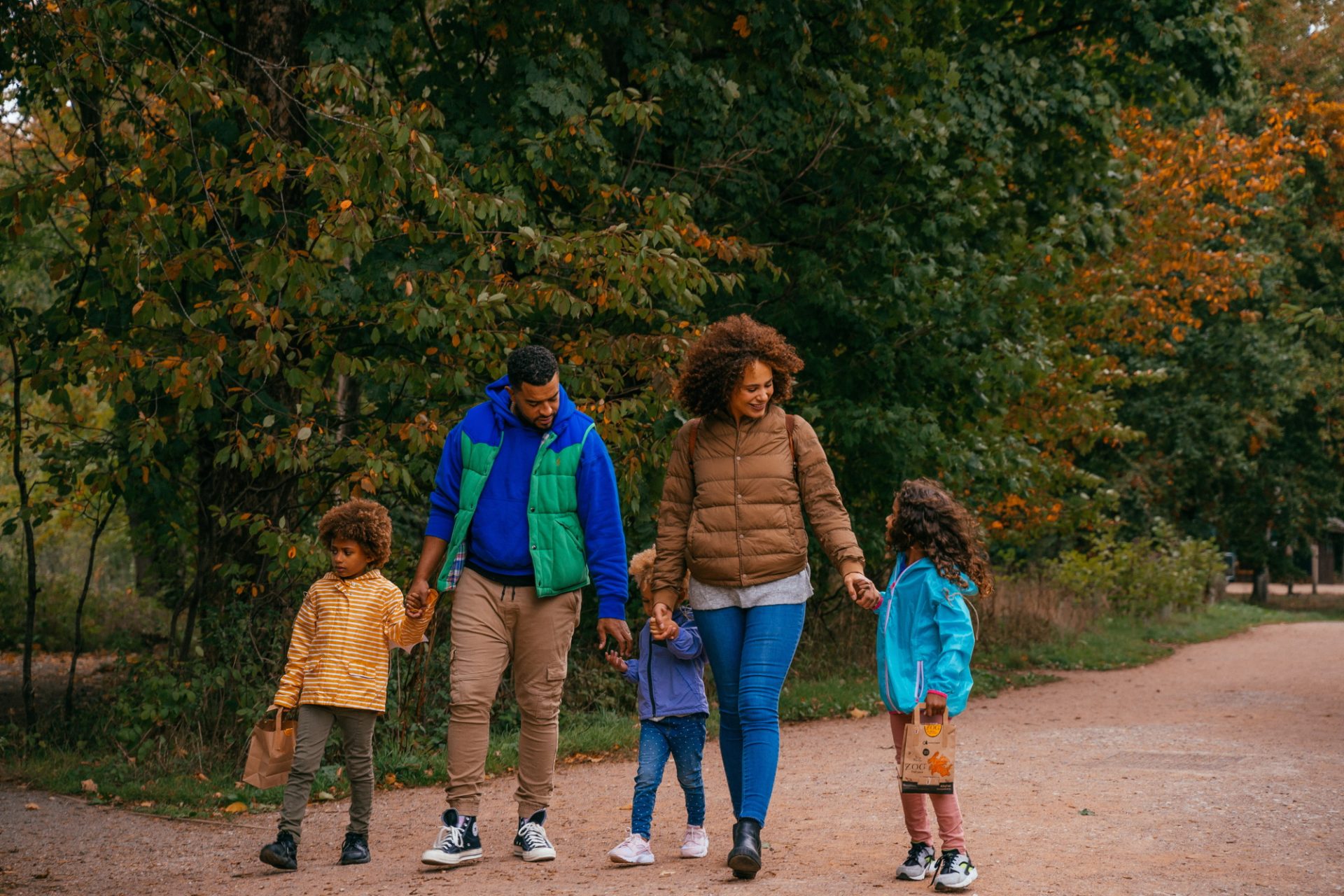 A family takes a walk in woodland. There are two adults and three children holding hands. 