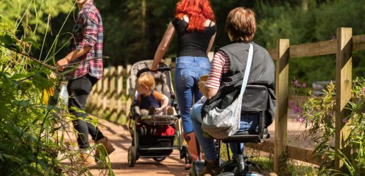 A family walk in a woodland. One of the people in the photograph uses a mobility device.