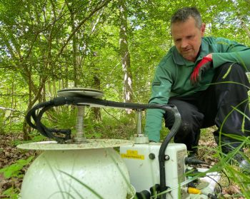 Matt Wilkinson inspects some machinery on the floor of a forest.