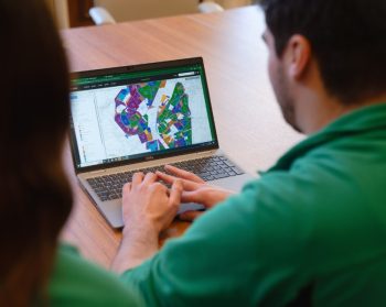 Two members of Forest Research inspect a map on a laptop screen, sat at a table.