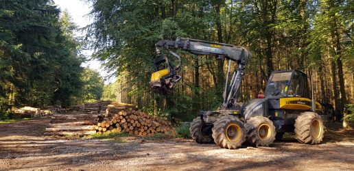 A large piece of forestery machinery next to some recently cut logs.